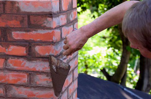 Mason reaching across a brick stack face with a loaded trowel