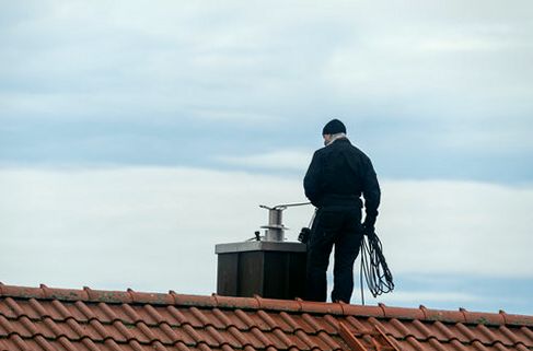 Chimney sweep standing on a tiled Durham roofline with his gear coiled